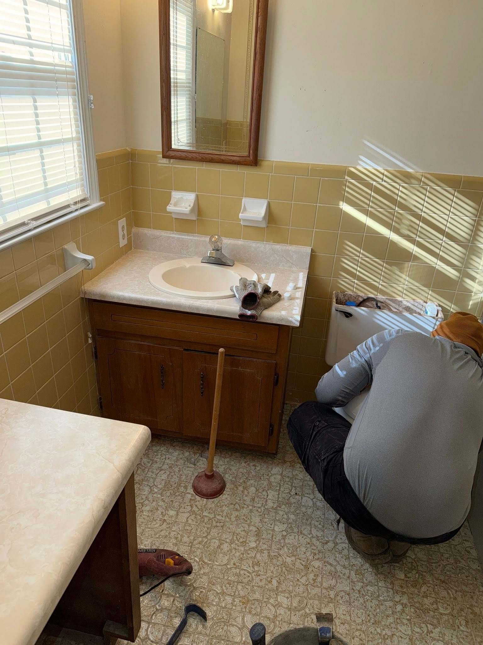 Bathroom before renovation — outdated 1970s yellow tile walls, old dark wood vanity and worn linoleum floor