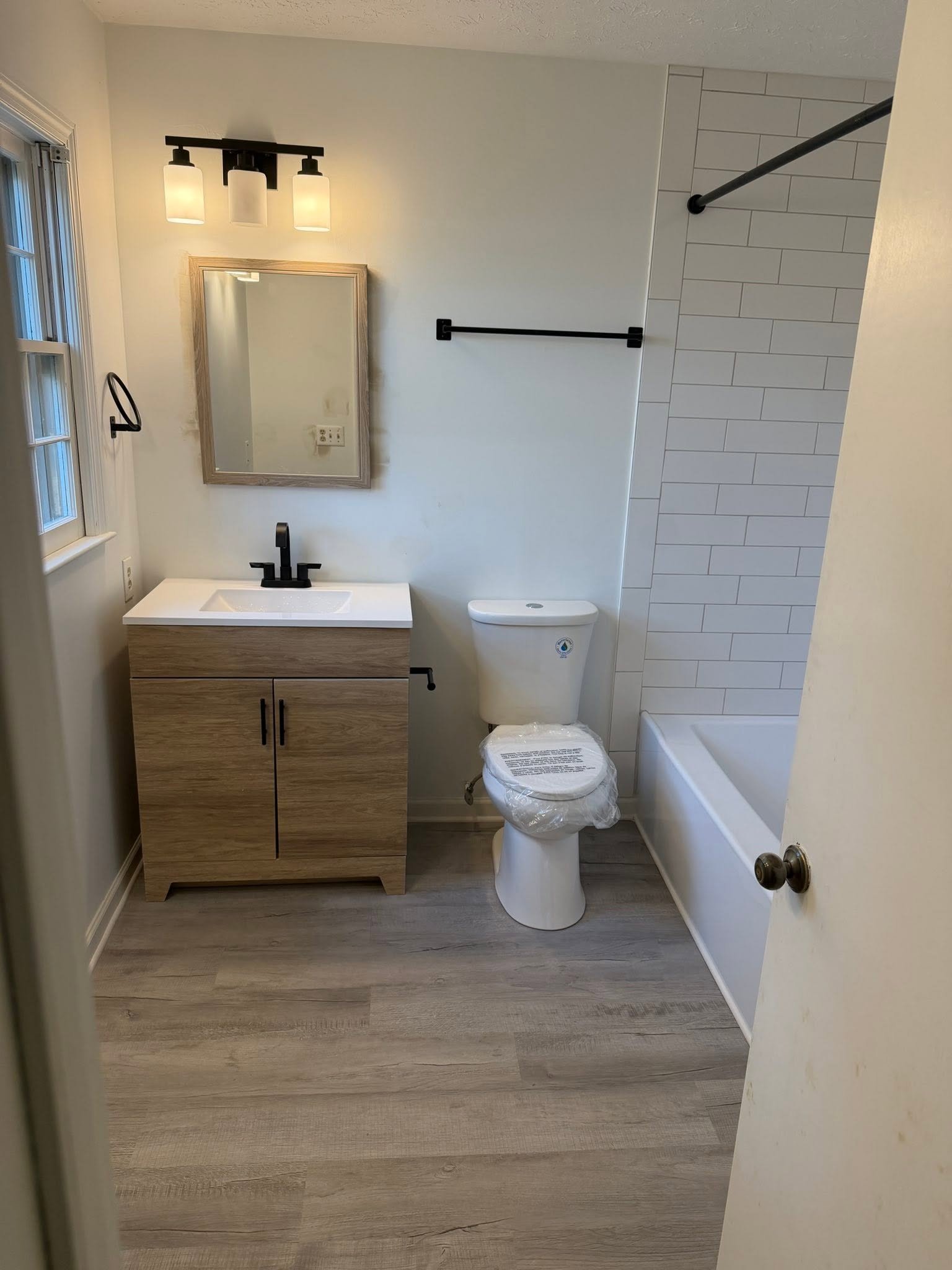 Bathroom after renovation — modern wood-look vanity, white subway tile tub surround, LVP flooring and matte black fixtures