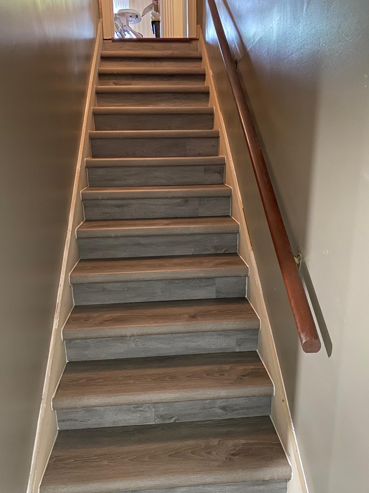 Staircase after LVP installation — full flight finished in grey wood-look luxury vinyl plank on treads and risers, clean and modern