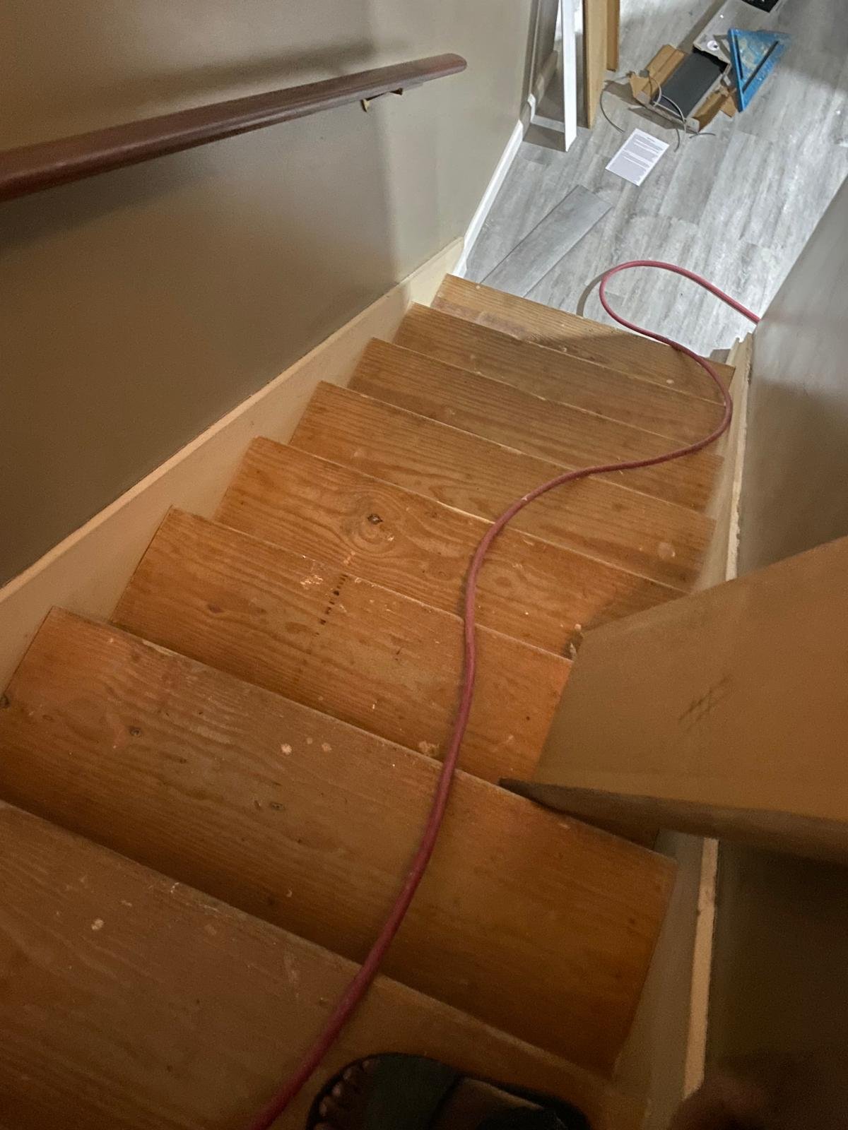 Staircase before renovation — bare plywood treads with no risers, red air hose on steps, rough unfinished wood
